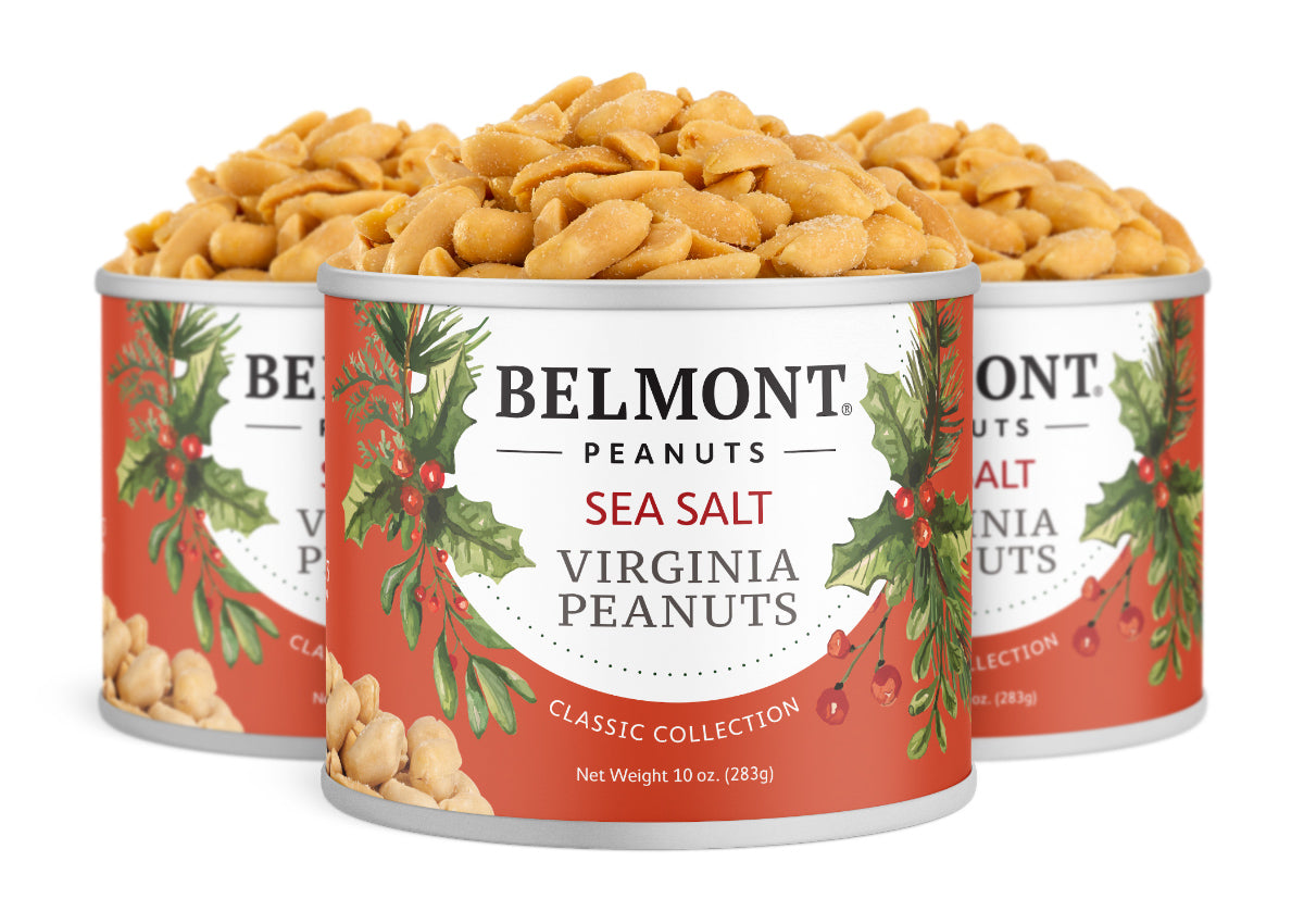 Three cans from the Belmont 10 oz. 3-Pack Holiday Sea Salt Peanuts are displayed together, featuring festive red and white labels with holly accents, and each filled with roasted sea salt peanuts.