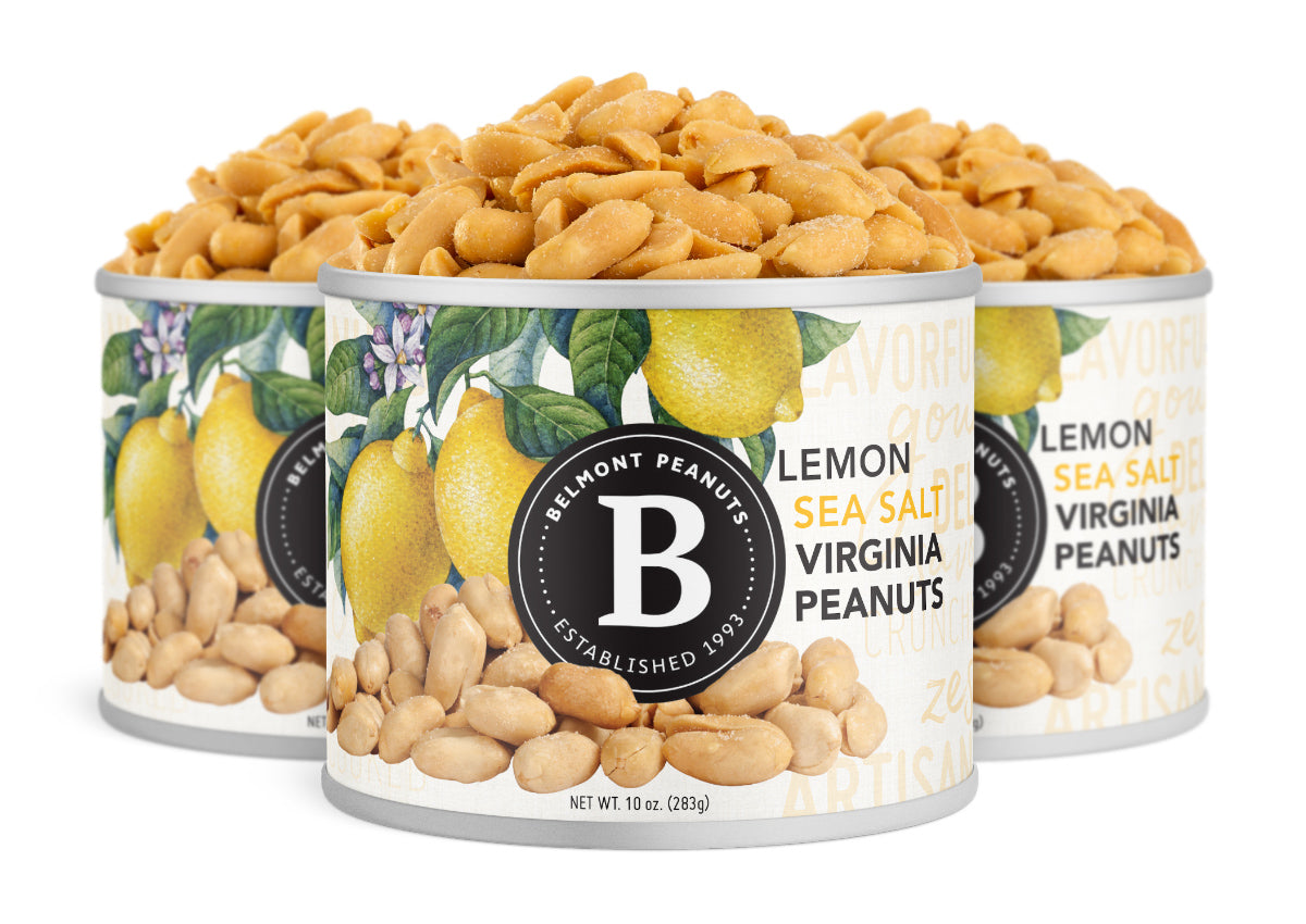 Three cans of Lemon Sea Salt Virginia Peanuts, decorated with bright lemon and peanut images, sit open and filled to the top with crunchy roasted peanuts.