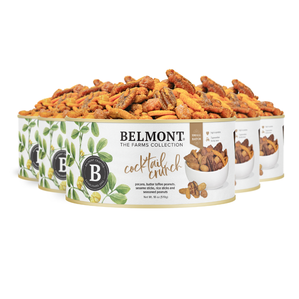 Six tins of Cocktail Crunch Mix, packed with seasoned peanuts and pecans, feature a white label with green leaves and a mixed nuts image. The tins, slightly overlapping in two rows, are filled to the top with assorted nuts.