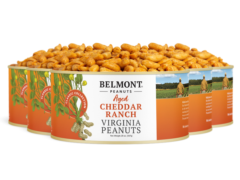Four cans of Aged Cheddar Ranch peanuts are lined up with open lids, showing the savory snack inside. Each can displays an orange label featuring peanuts and a field.