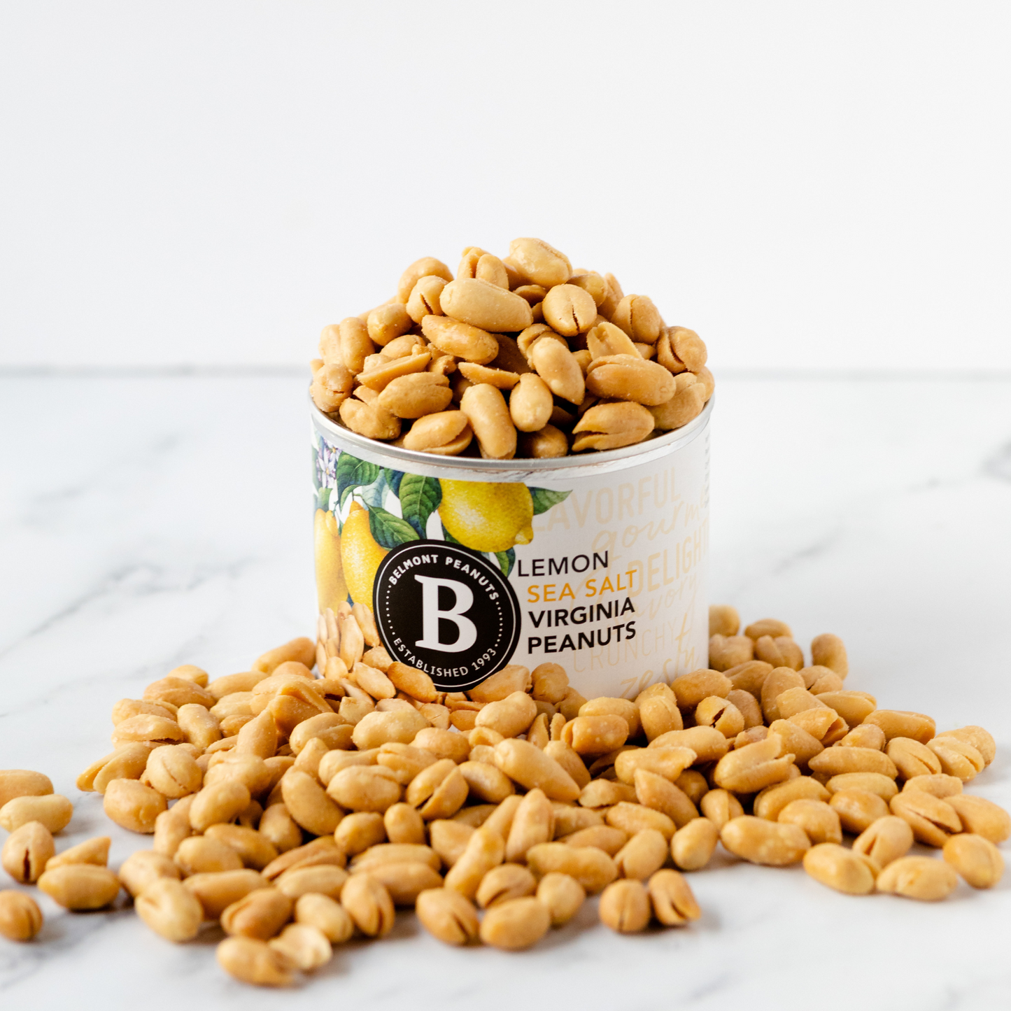 A can labeled Lemon Sea Salt is filled with Virginia Peanuts, which are also scattered around the base on a white surface.