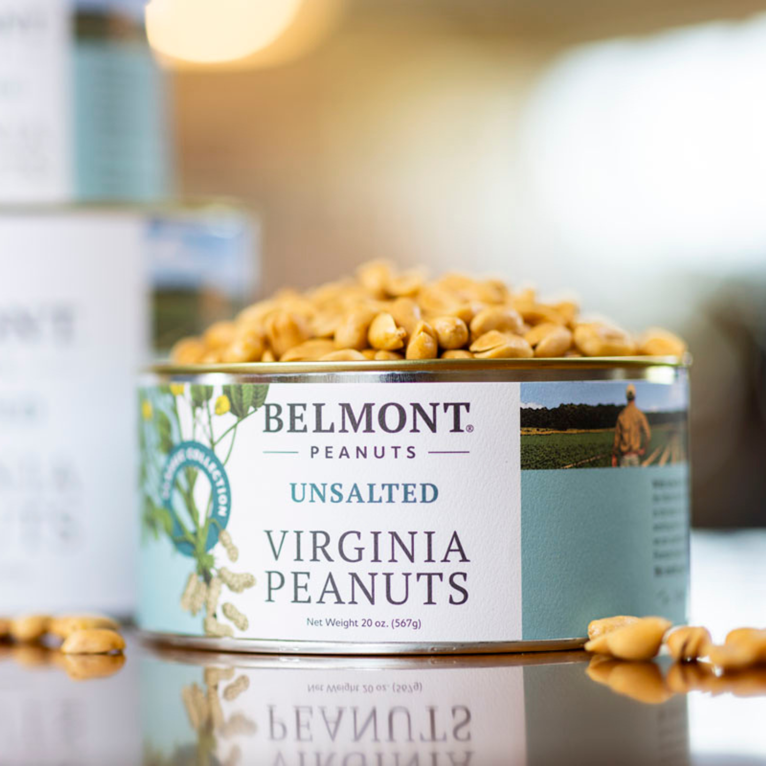 An open can of Belmont Peanuts labeled "Unsalted" overflows with no salt added peanuts, spilling out. The label displays peanut images and a photo of a person standing in a field.