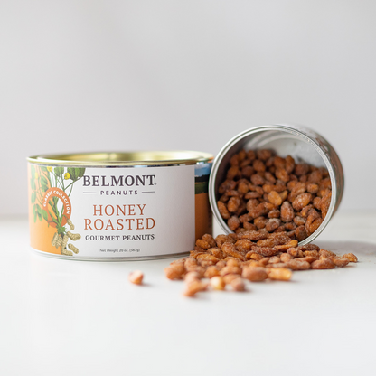 A can of Honey Roasted peanuts rests on its side, with jumbo honey roasted peanuts spilling invitingly onto a white surface in front of the open container.