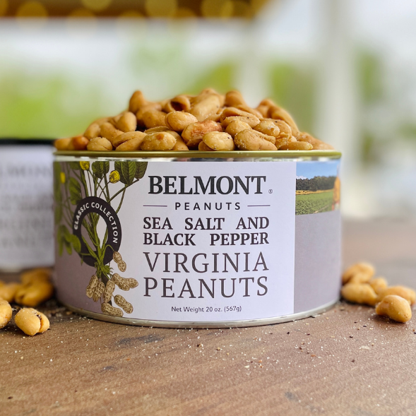 An open can labeled "Sea Salt & Black Pepper" contains gourmet Virginia peanuts spilling onto a rustic wooden surface; its label displays peanuts and green fields in the background.