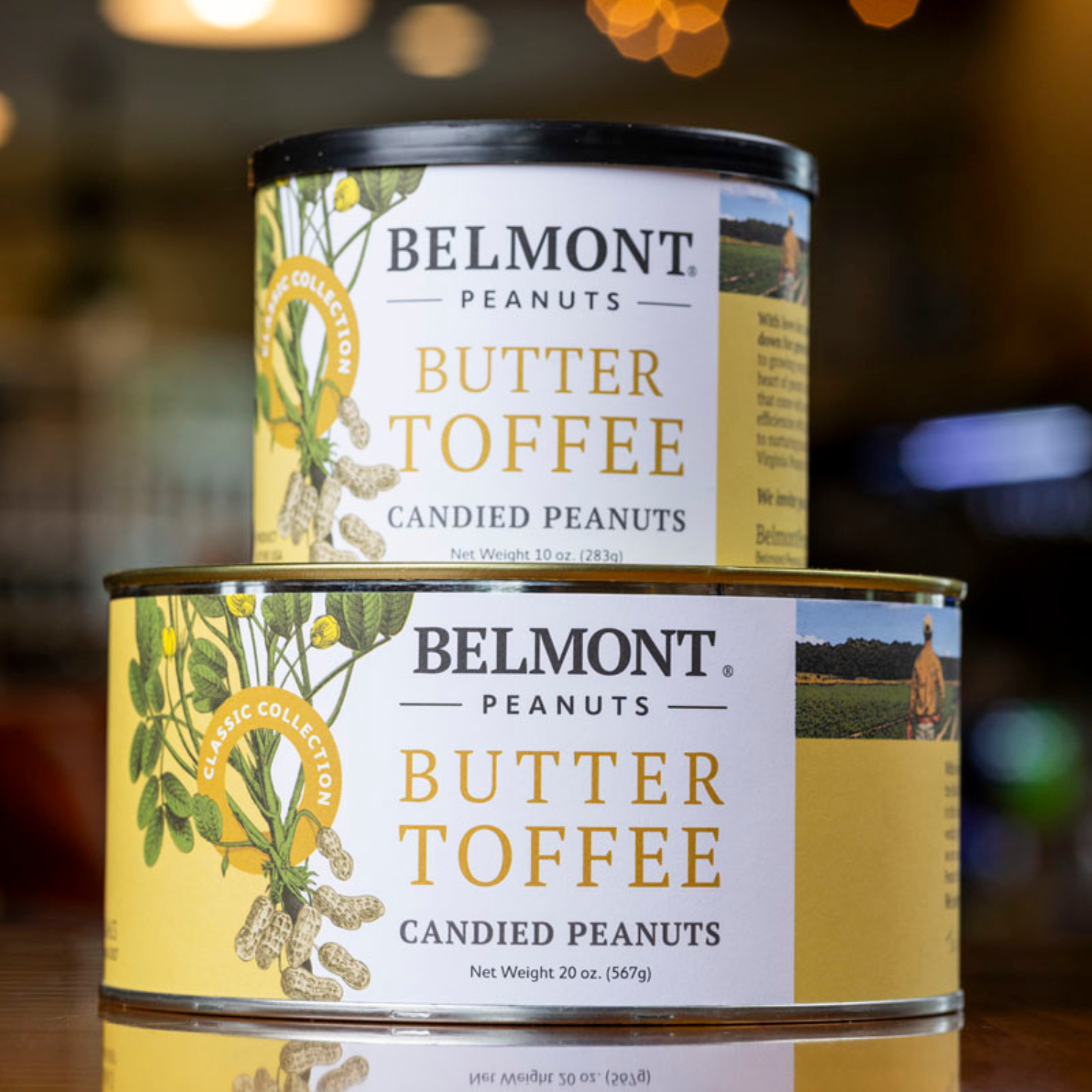 Two stacked cans of Butter Toffee peanuts with yellow labels and peanut illustrations stand out against a softly lit, blurred background, highlighting their sweet candy and buttery coating appeal.