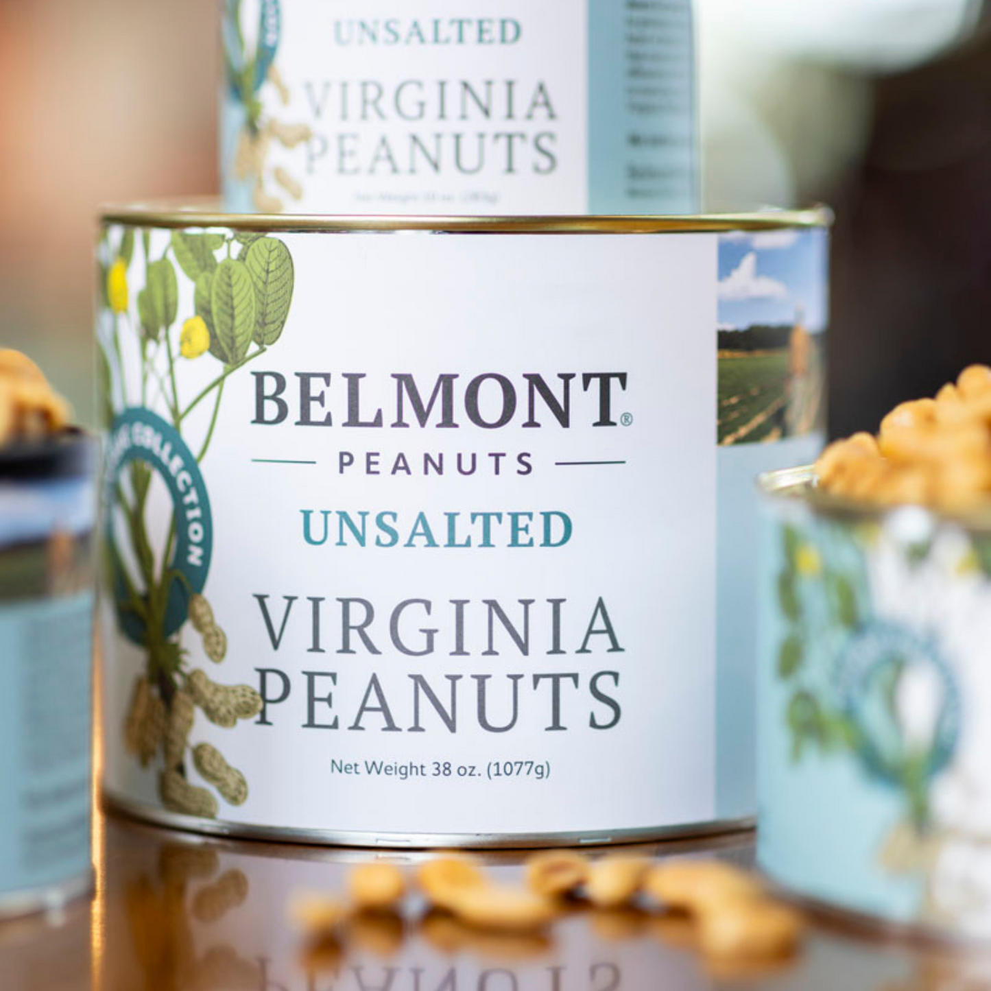 A can of Unsalted Belmont Premium Peanuts sits on a wooden surface, with peanuts and another can partially visible behind it. The label notes no salt added and a net weight of 38 oz (1077g).
