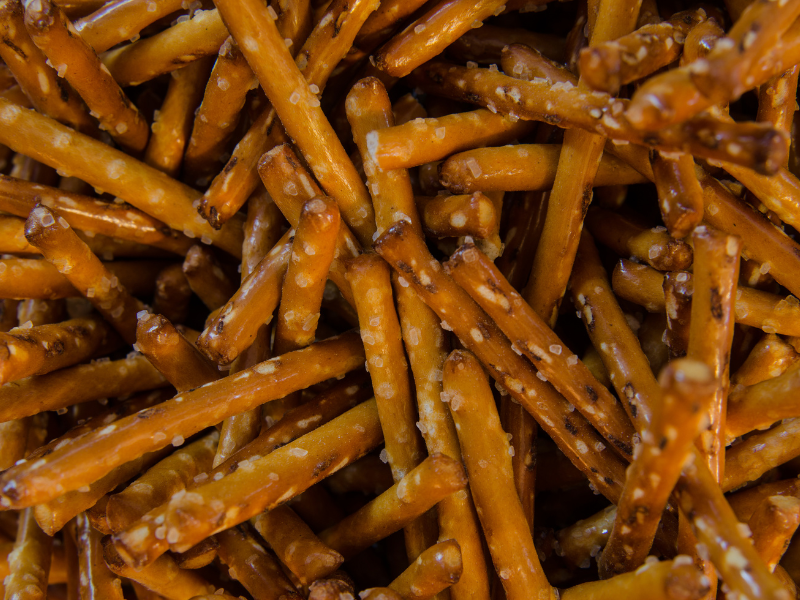 A close-up view of Dill Pickle Pretzel Sticks, showing their golden-brown hue, coarse salt, and a zesty dill seasoning.