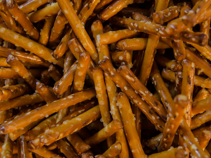 A close-up view of Dill Pickle Pretzel Sticks, showing their golden-brown hue, coarse salt, and a zesty dill seasoning.