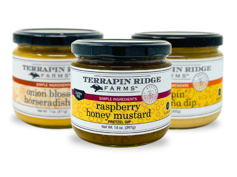 A jar of Raspberry Honey Mustard by Terrapin Ridge Farms is featured in front, with two other Terrapin Ridge Farms gourmet condiment jars—Onion Blossom Horseradish Dip and Sriracha Horseradish Dip—blurred in the background.