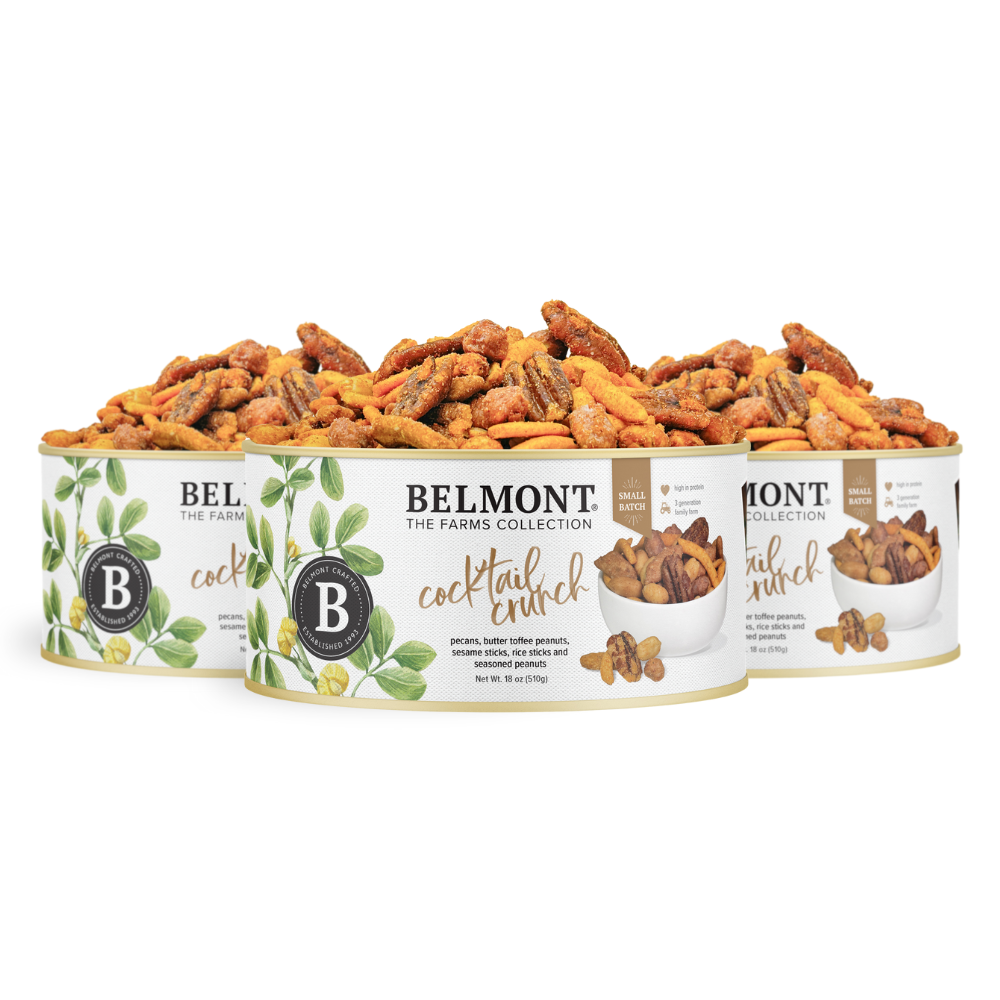 Three cans of Cocktail Crunch Mix, packed with pecans, butter toffee candied peanuts, and assorted nuts, are set in a row. The white cans display green leaf graphics and product images on the labels.