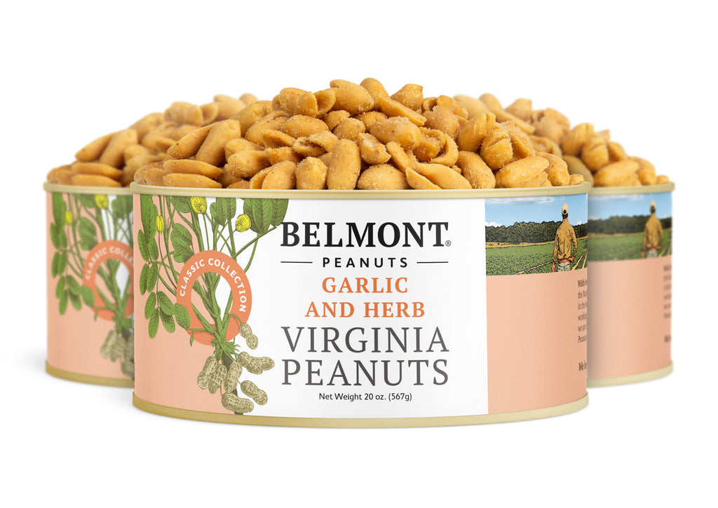 Three cans of Garlic & Herb gourmet Virginia peanuts are shown, with peanuts piled high above them. The label displays illustrated peanut plants and a farmer’s photo—a delicious protein snack.