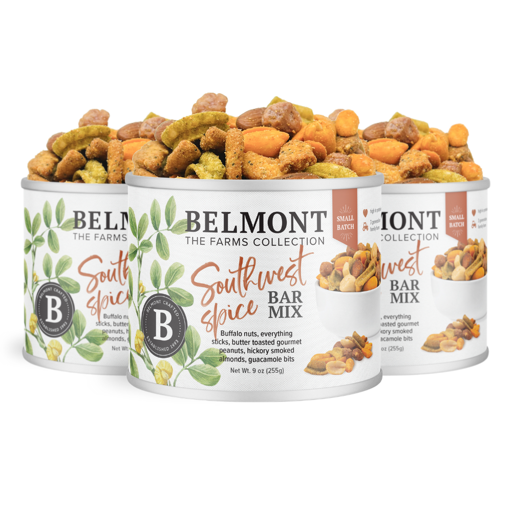 Three cans of Southwest Spice Bar Mix, each with a white label featuring green leaves and snack images, are stacked in a triangle. The mix includes gourmet peanuts and snacks in a colorful blend.