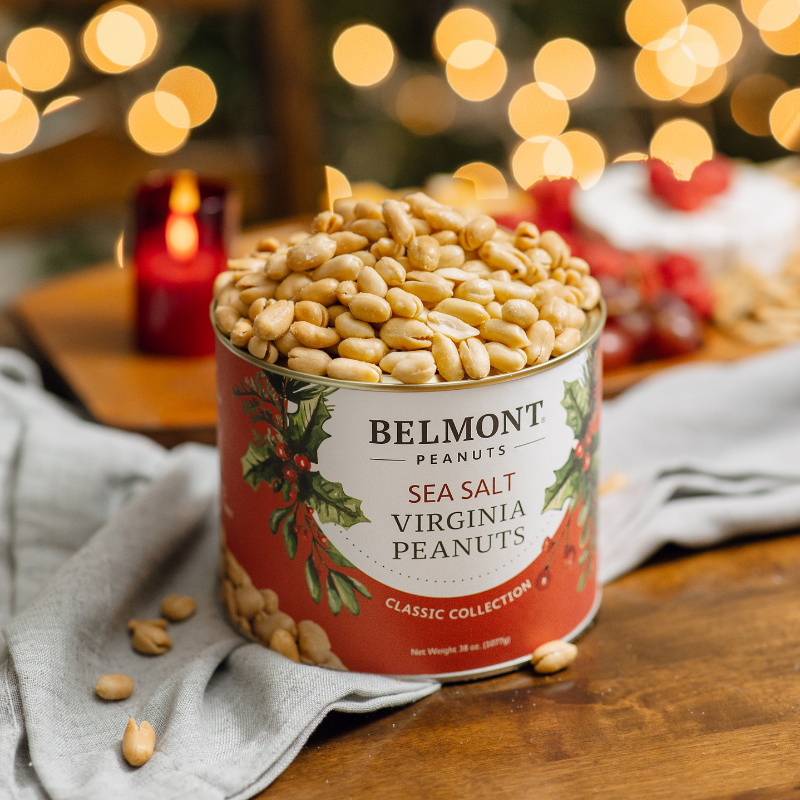 Can of Belmont Peanuts with festive design on a wooden table with blurred lights in the background