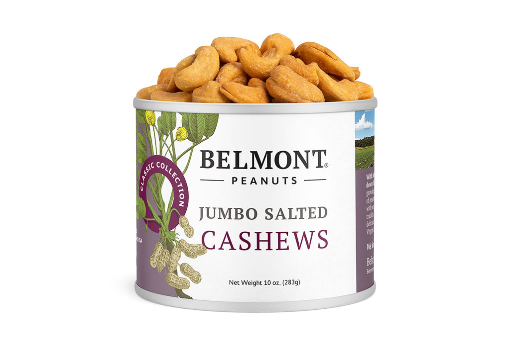A 10 oz can of Jumbo Salted Cashews with golden roasted cashews spilling out of the open top—a delicious, healthy snack for any occasion. The white label features purple accents and a peanut plant illustration.